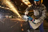 A person wearing safety equipment grinds metal, creating a shower of bright sparks.