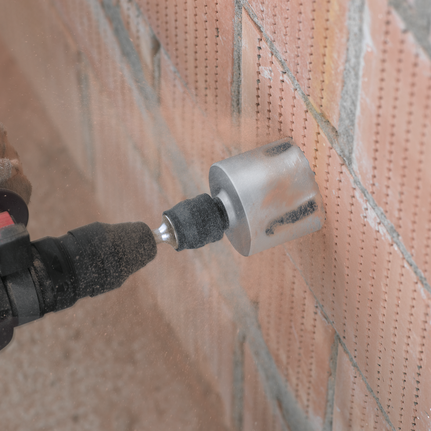 Rotary drill with a hole saw attachment cutting into a brick wall.
