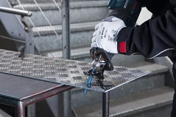 Person wearing safety equipment cuts metal sheet with a reciprocating saw.