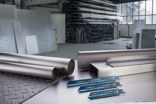 Metal pipes, metal sheets, and saw blades arranged on a worktable in an industrial workshop.