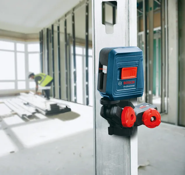 A person wearing safety equipment works in a building frame near a mounted laser leveling tool.