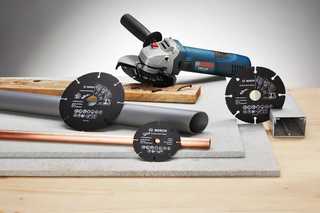 Angle grinder with several cutting discs displayed next to metal and plastic pipes on a workbench.