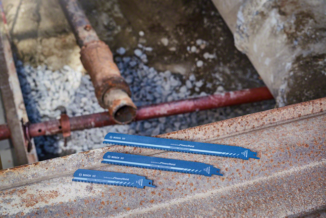 Three blue reciprocating saw blades are placed on a rusted steel beam at a construction site.