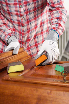 Person wearing safety equipment sanding a wooden cabinet with a sanding sponge.