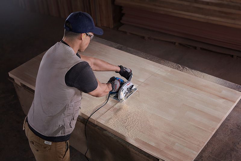 A person wearing safety equipment cuts wood with a hand-held circular saw.