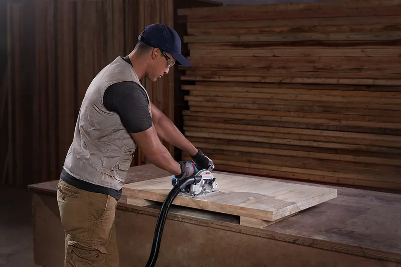 A person wearing safety equipment cuts a wooden board with a circular saw.
