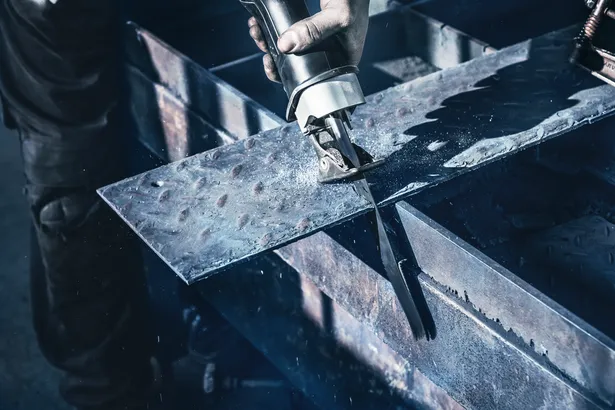 Person using a reciprocating saw to cut a metal sheet.