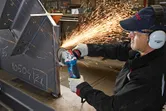 A person wearing safety equipment grinds metal with an angle grinder, creating sparks.