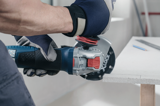 A person wearing safety equipment uses an angle grinder to cut a board.