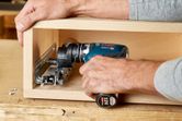 Person using a cordless drill to install a metal drawer slide inside a wooden box.