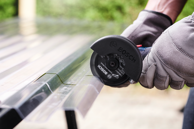 Person wearing safety equipment uses an angle grinder to cut a metal profile.