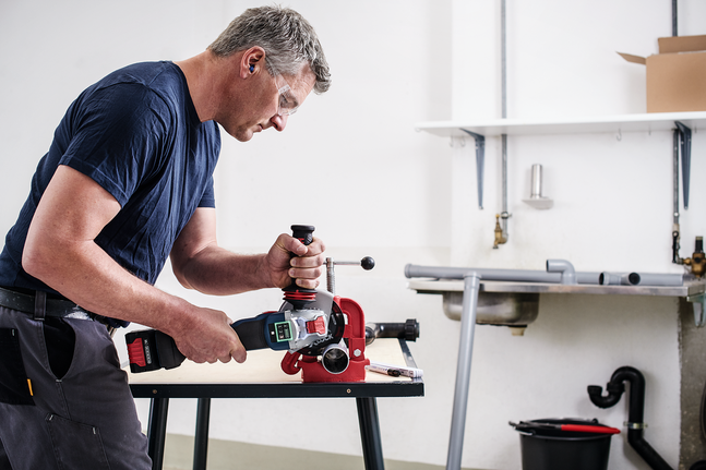 Person wearing safety equipment uses a cordless power tool on a red pipe vise.