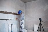 A person wearing safety equipment aligns wall tiles using a laser leveling tool.