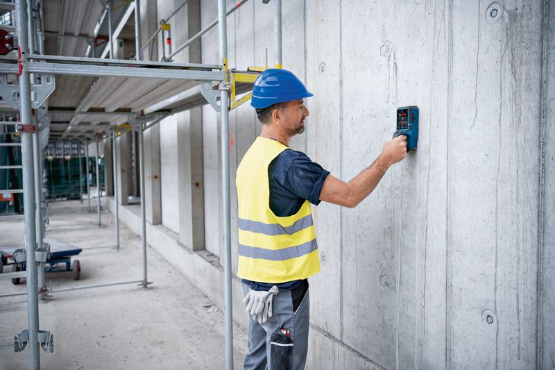 Person wearing safety equipment scans a concrete wall with a detector tool.