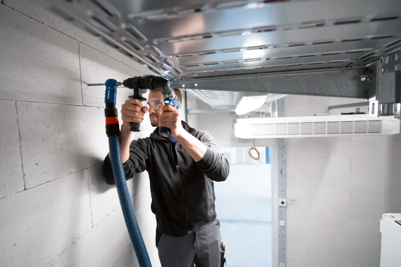 A person wearing safety equipment uses a FlexiClick Adapter to drill into a concrete wall.