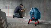 A person aligns tiles on a wall using a laser leveling tool.