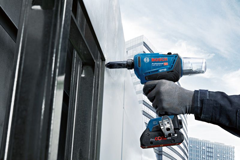 A person wearing safety equipment fastens a metal panel with a cordless rivet gun.