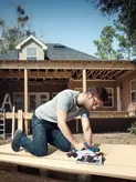 A person wearing safety equipment cuts wood on a construction site with a cordless circular saw.