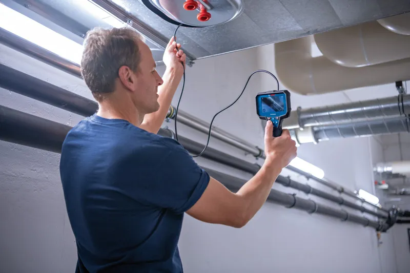 A person inspects inside an air duct using an inspection camera.