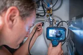 A person uses an inspection camera to examine pipes inside a cabinet.