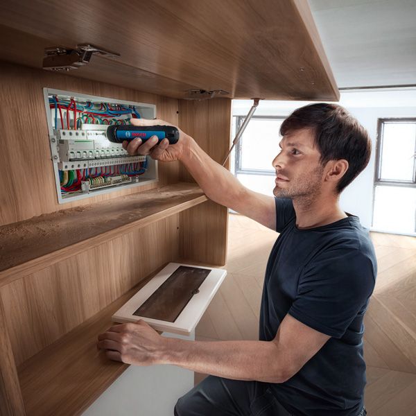 A person secures wires in an electrical panel using a cordless screwdriver.