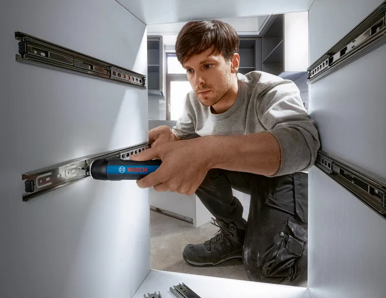 A person installs drawer slides in cabinetry using a cordless screwdriver.