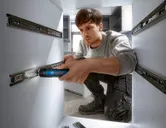 A person installs drawer slides in cabinetry using a cordless screwdriver.