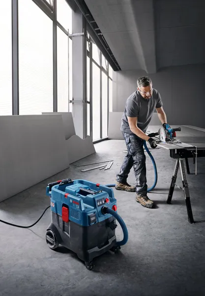 A person wearing safety equipment cuts a board on a stand, using an all-purpose extractor.