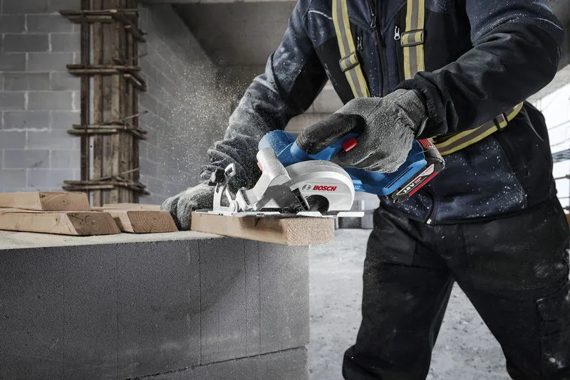 A person wearing safety equipment cuts lumber with a circular saw on a construction site.