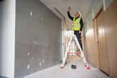 A person wearing safety equipment marks a ceiling using a laser leveling tool.