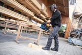 A person wearing safety equipment uses a cordless chainsaw to cut wood blocks.