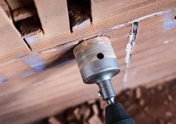 A rotary tool with a hole saw attachment drills into a brick wall.