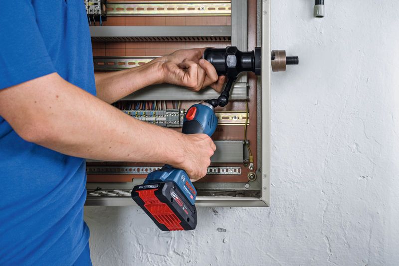 A person uses a cordless hydraulic punching tool on an electrical panel.