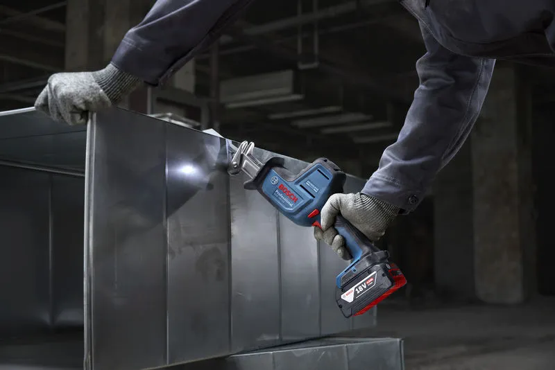 A person wearing safety equipment cuts sheet metal with a cordless reciprocating saw.