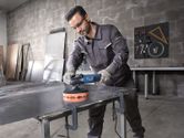 A person wearing safety equipment polishes a metal sheet with a power tool.