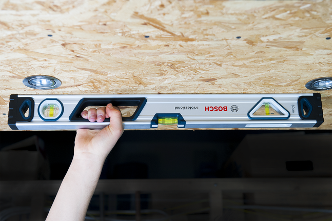 Person holds a spirit level against a wooden ceiling panel.