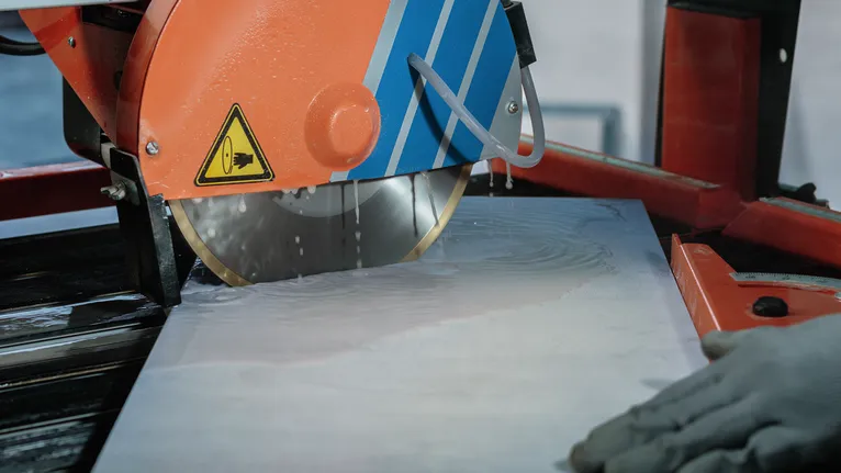 A person wearing safety equipment cuts a wet tile using a large circular saw.