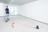 A person operates a laser leveling tool projecting lines across an empty room.