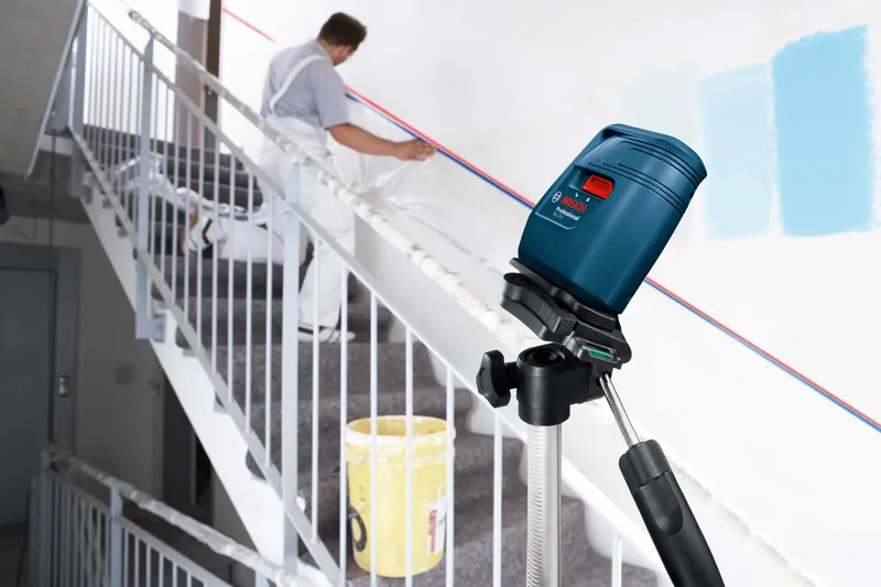 Laser leveling tool projecting lines on a stairwell wall, person preparing for painting.