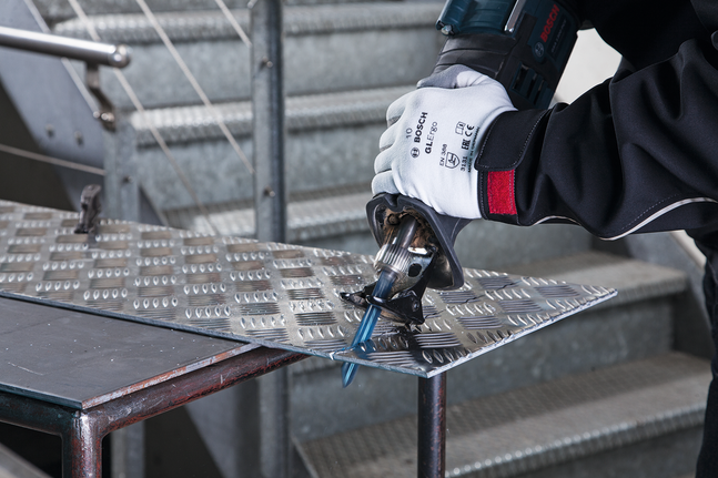 Person wearing safety equipment cuts metal sheet with a reciprocating saw.