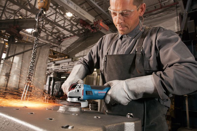 A person wearing safety equipment grinds metal with an angle grinder, producing sparks.