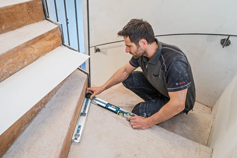 A person measures the angle of a stair step using an angle measurer.