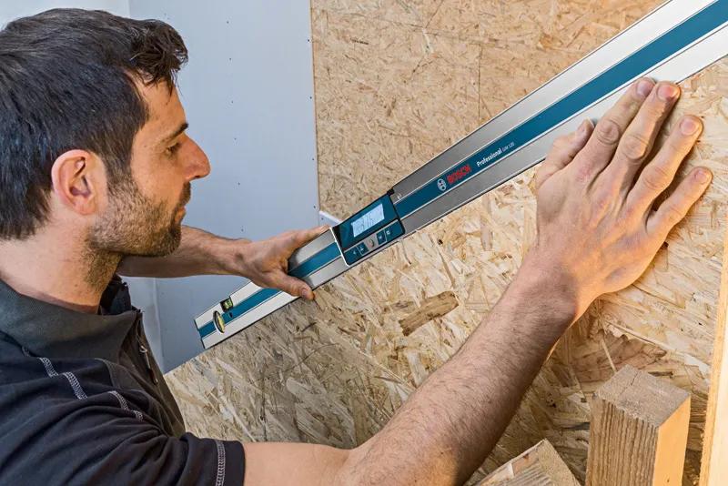 Person using a digital inclinometer to measure the angle of a wooden surface.