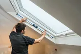 Person measuring window angle with a digital inclinometer in a finished attic room.
