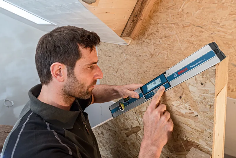 A person uses a digital inclinometer to measure the angle of a wooden structure.