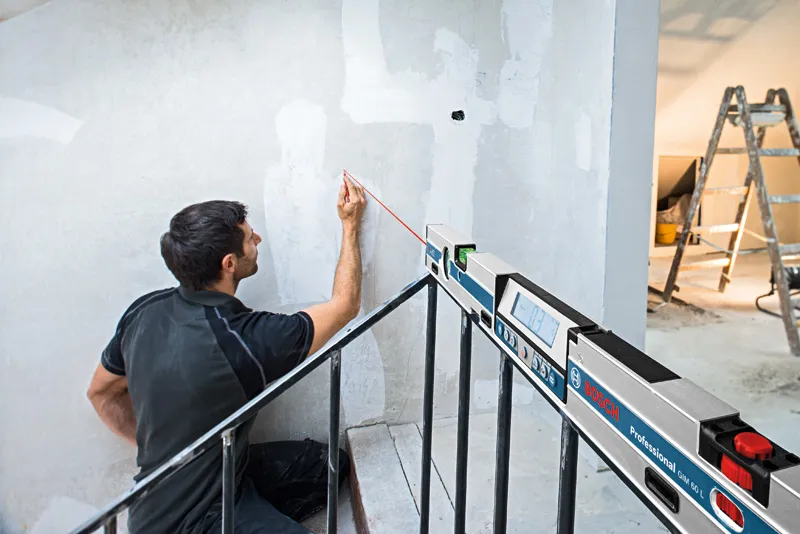 A person marks a wall using a digital inclinometer projecting a straight laser line.