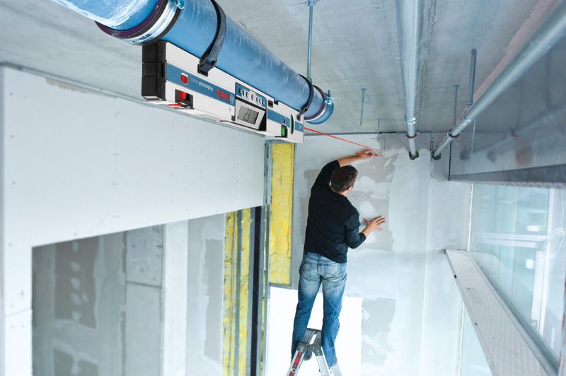 A person on a ladder marking a wall using a digital inclinometer for alignment.