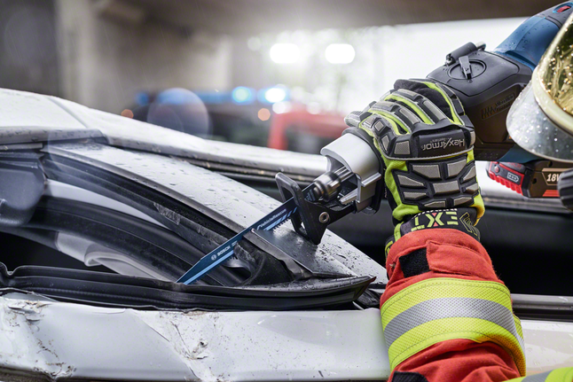Person wearing safety equipment cuts through a damaged car windshield with a reciprocating saw.