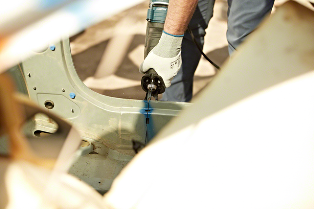 Person wearing safety equipment uses a reciprocating saw to cut metal in a vehicle frame.