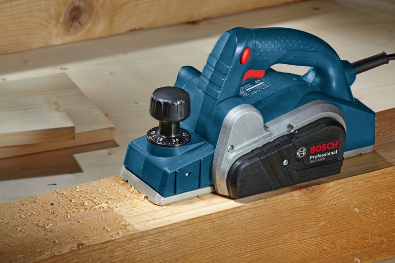Planer smoothing the surface of a wooden beam on a workbench.